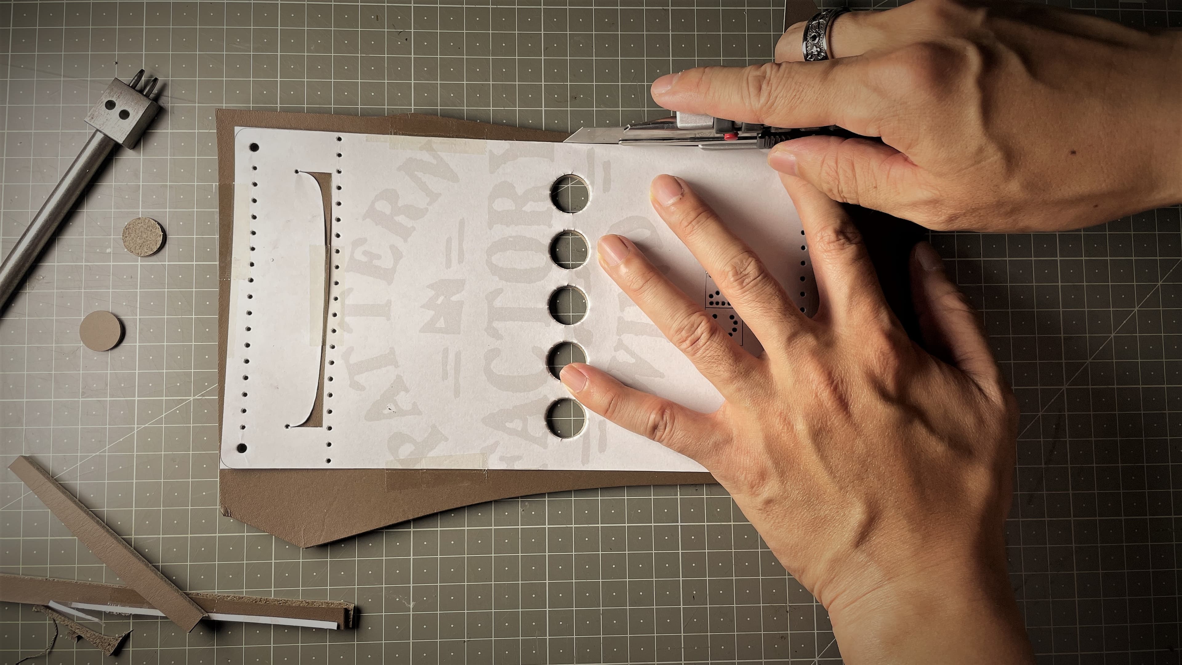 Hands cutting a leathercraft pattern on a gridded work surface